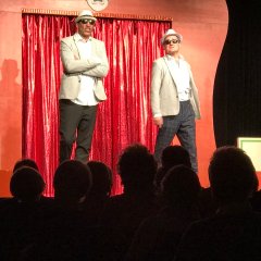 In der Zirkusmanege sieht man zwei Kabarettisten verkleidet als Mafia-Bosse mit weißen Anzügen, Hut und Sonnenbrille.