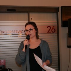 Moderatorin Theresa Altrogge mit Mikrophon in der Hand. Sie ist jung, dunkelhaarig und trägt eine Brille.