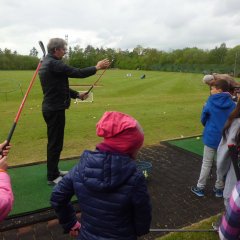 Der Trainer zeigte den Kindern die richtige Haltung des Golfschlägers.