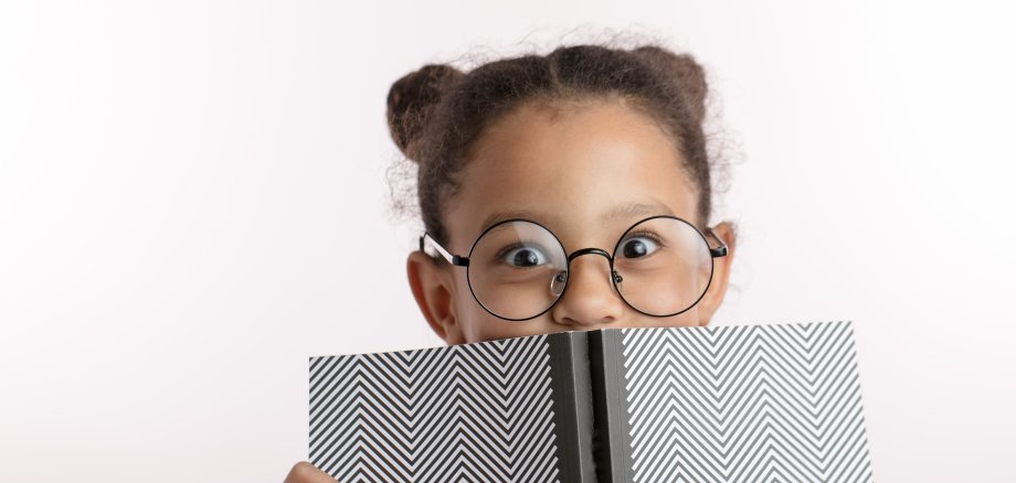 clever little girl with hairbunds and round glasses hiding behind the notepad