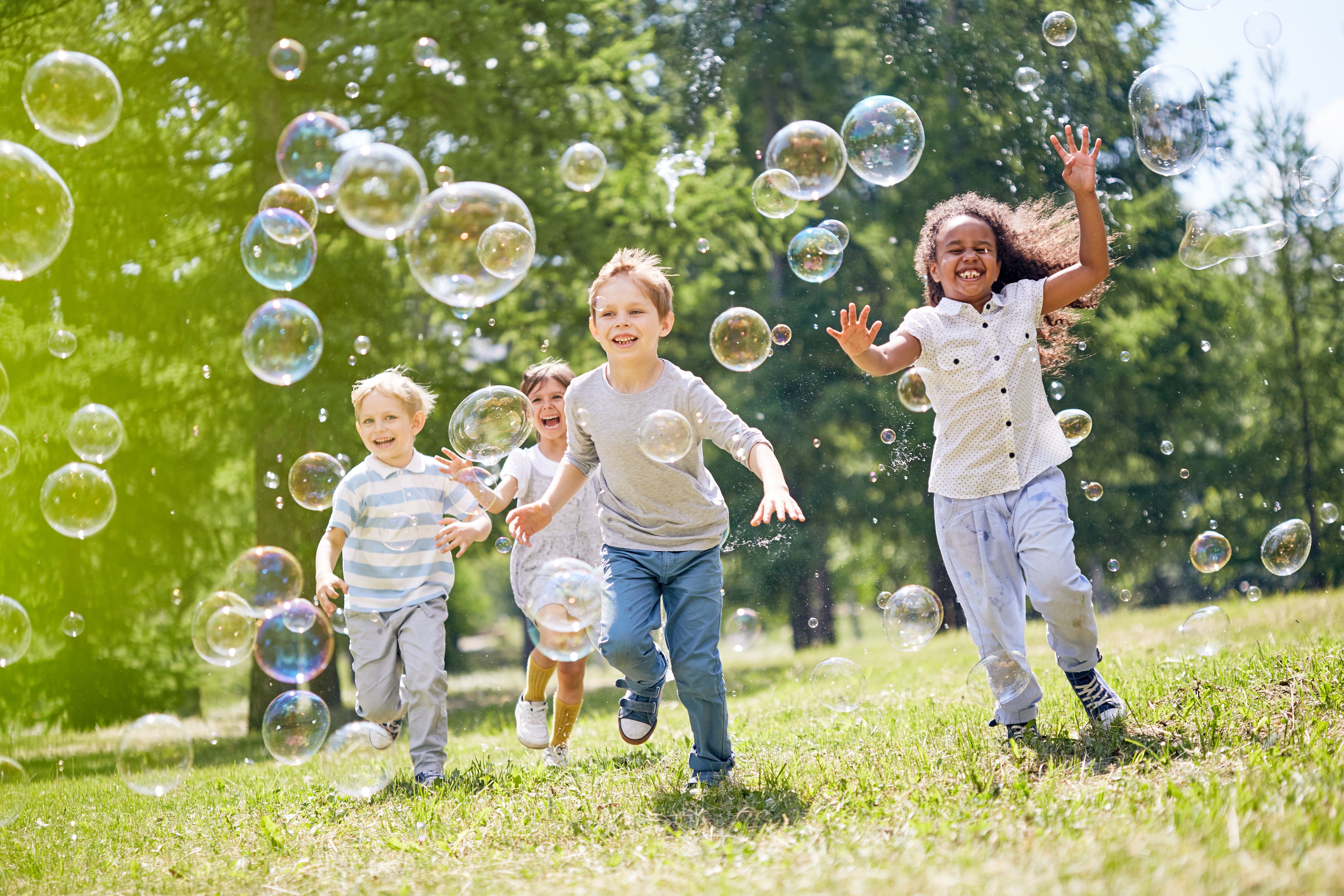 Spielende Kinder mit Seifenblasen auf einer Wiese.