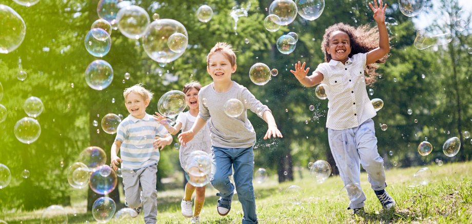 Spielende Kinder mit Seifenblasen auf einer Wiese.