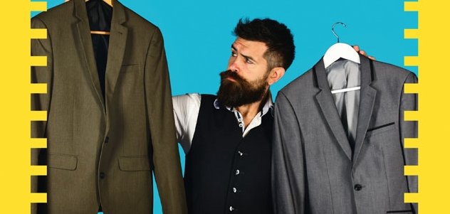 Ein Mann mit Vollbart hat zwei Jacketts auf dem Bügel in der rechten und der linken Hand. Er schaut kritisch und fragend auf ein Jackett.