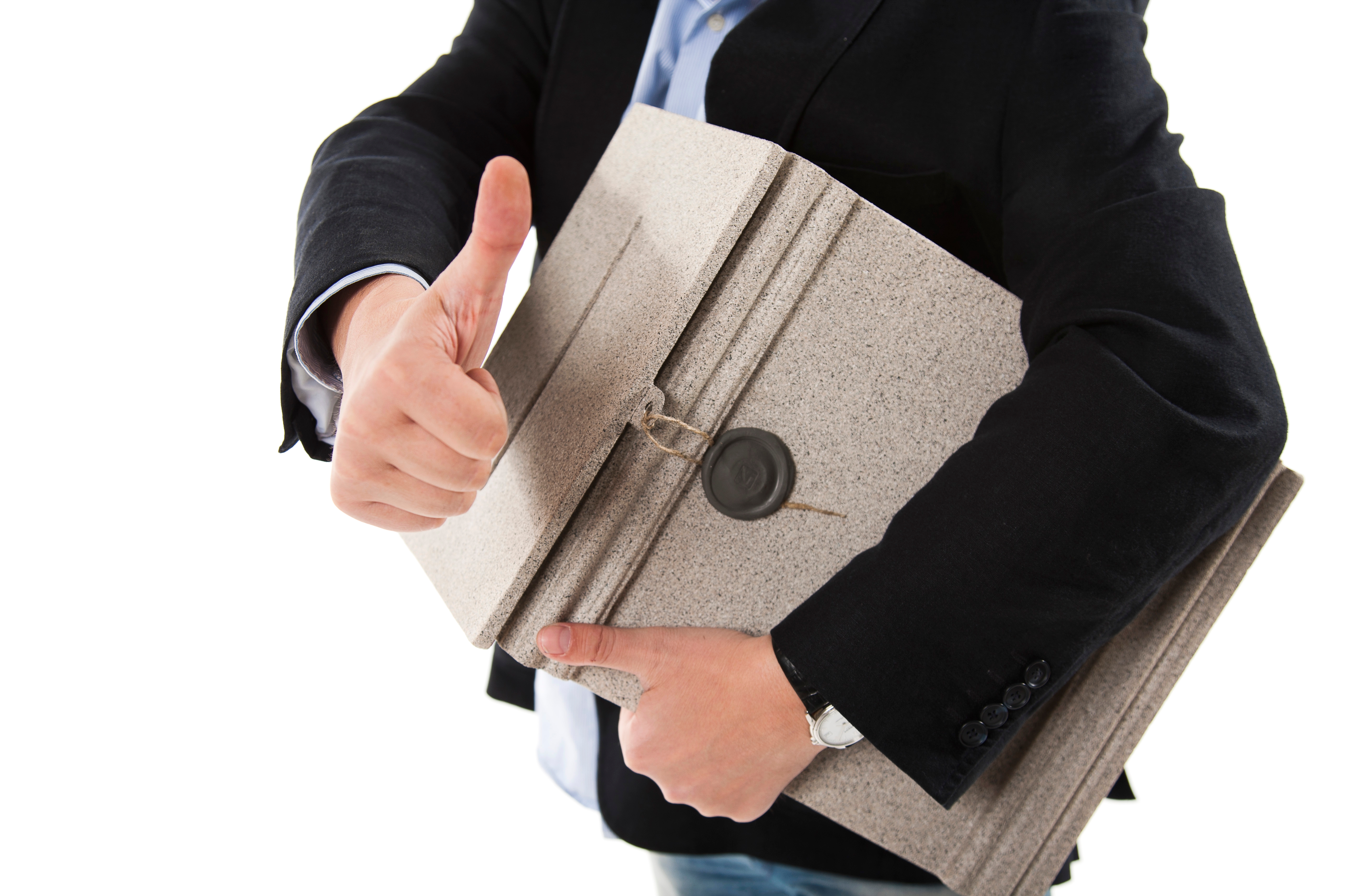 Auf dem Foto ist ein männlicher Wahlhelfer in einem hellblauen Hemd und einem dunkelblauen Jackett zu sehen, der eine versiegelte, hellgraue Wahlurme unter dem Arm trägt. Der Wahlhelfer hat die rechte Faust ausgestreckt und hält als Geste der Zustimmung seinen Daumen nach oben. Am linken Arm trägt er eine schwarze Herren-Armbanduhr aus Leder. Der Hintergrund ist komplett Weiß.