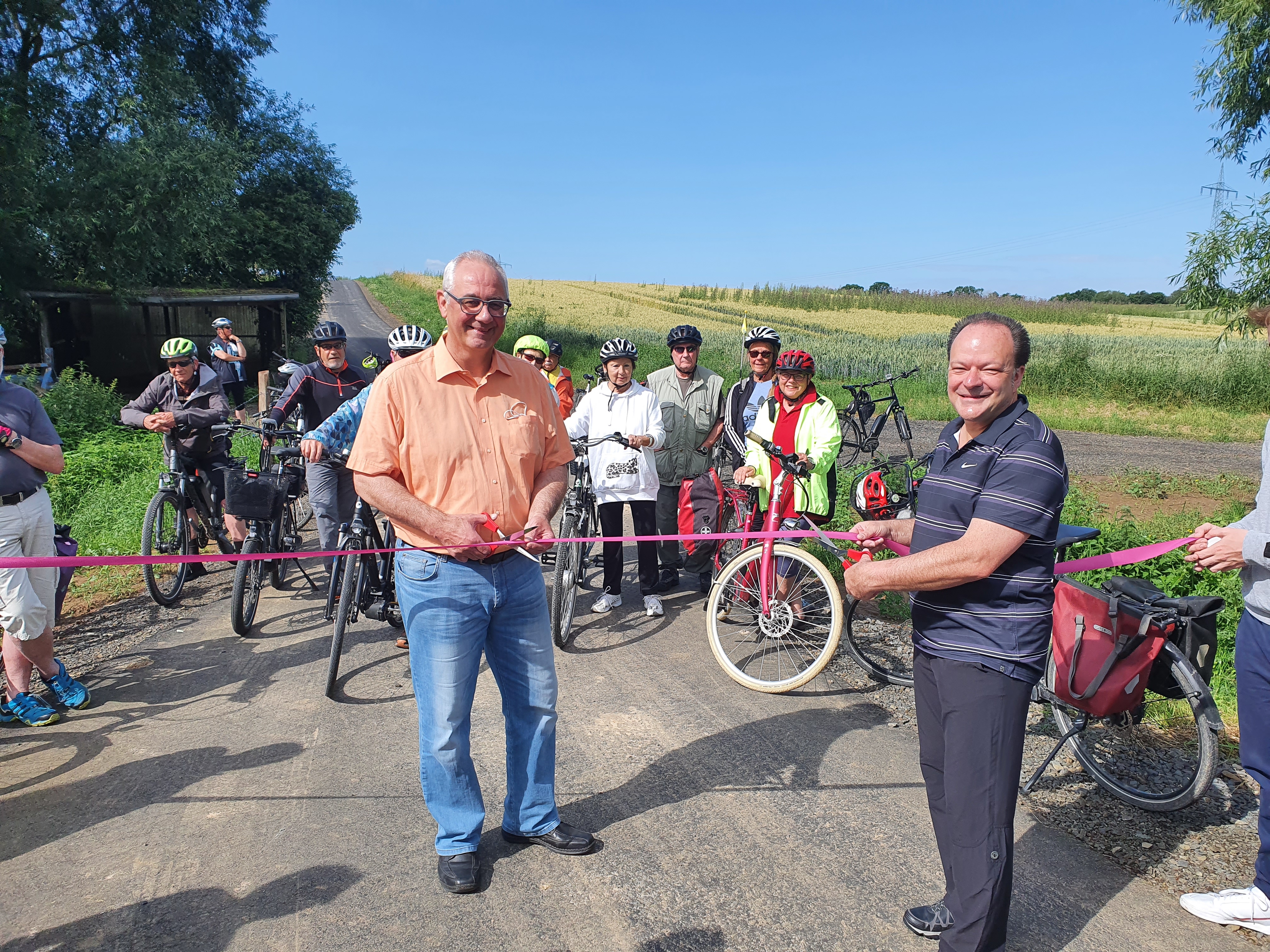 Das Band wird durchschnitten und der neue Radweg ist eingeweiht: Bürgermeister der Gemeinde Lohfelden Uwe Jäger (l.) und Bürgermeister der Gemeinde Kaufungen Arnim Roß würdigen den reibungslosen Ablauf des Gemeinschaftsprojektes und begrüßen den Radwegelückenschluss zwischen den beiden Gemeinden. Im Hintergrund die Lohfeldener Teilnehmerinnen und Teilnehmer.