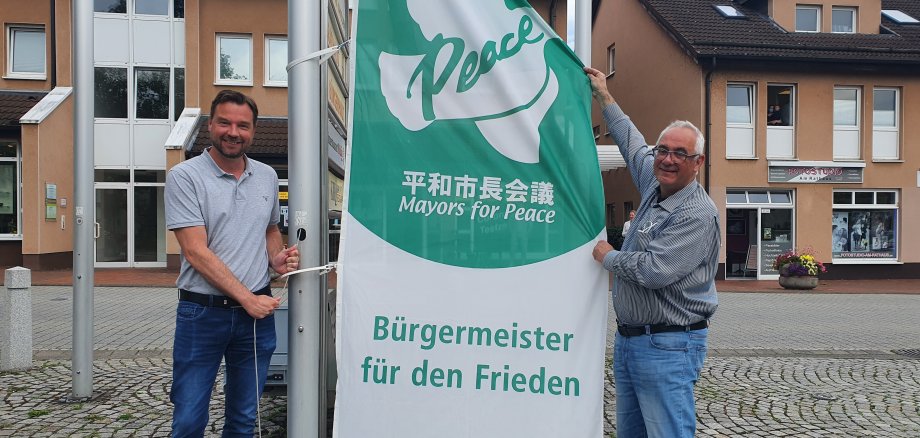 Bürgermeister der Gemeinde Lohfelden, Uwe Jäger (r.), hisste zusammen mit Leiter des Fachbereichs Verwaltung und Ordnung, Kai Hast, die Mayors for Peace-Flagge. 
