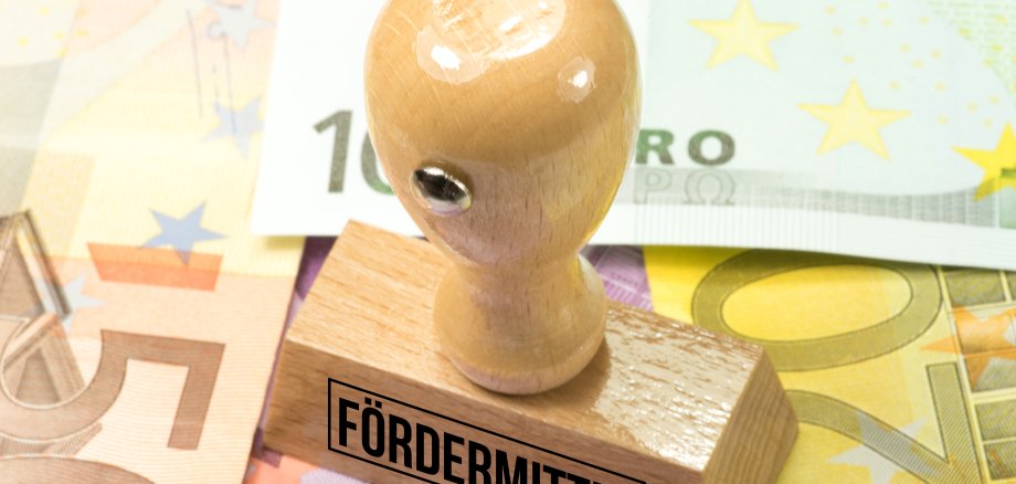 Auf dem Foto sind Euro Geldscheine und ein Stempel mit dem Aufdruck Fördermittel zu sehen.