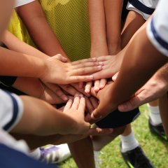 Auf dem Foto sind die vereinten Hände von einer Gruppe junger Fußballspielender zu sehen.