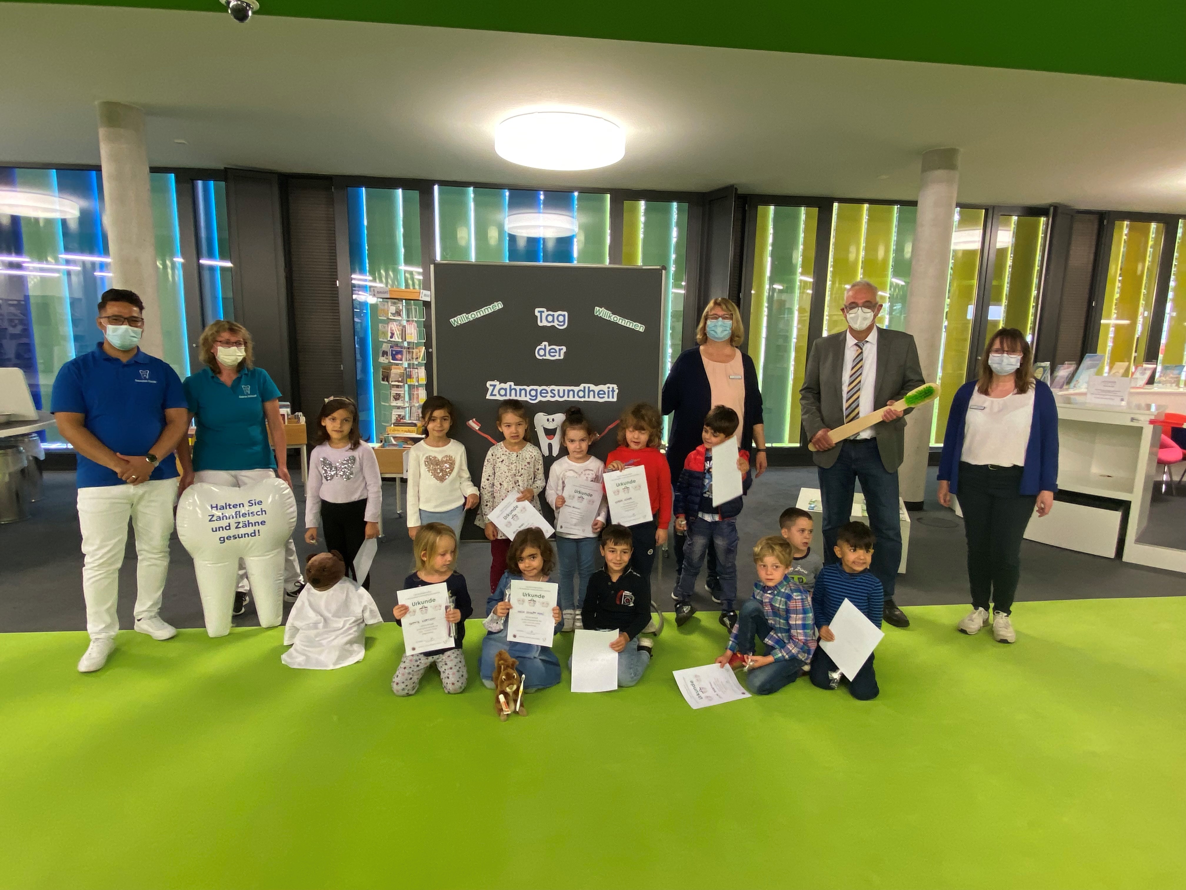 Zahnarzt Samiullah Habibi und seine Assistentin Gudrun Schmidt (links der Pinnwand) Bürgermeister Uwe Jäger und Büchereimitarbeiterinnen Gabriele Nemenz und Michaela Fenn (rechts der Pinnwand), mit den Kindern der Kindertagesstätte des ASB beim „Tag der Zahngesundheit“ in der Gemeinde- und Schulbücherei Lohfelden.