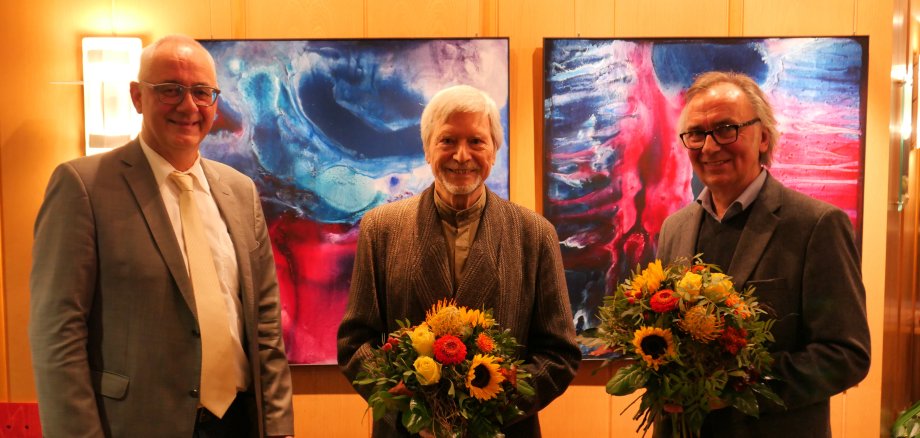 Bürgermeister Uwe Jäger (l.) bedankte sich mit einem Blumenpräsent für die gelungene Ausstellungseröffnung bei den Künstlern Prof. Dr. Gernot Minke (M.) und Wolfgang Loewe.