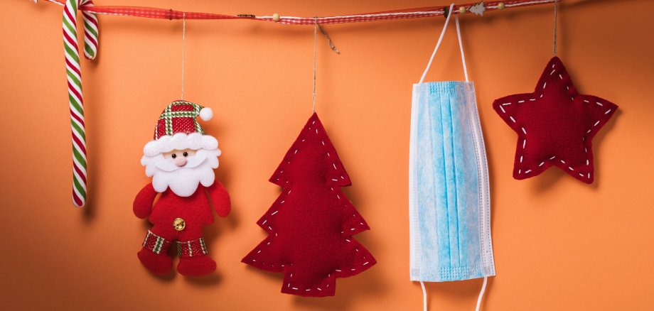 Auf dem Foto ist eine Weihnachtsdekoration, zu der auch eine hellblaue medizinische Atemschutzmaske gehört, zu sehen. 