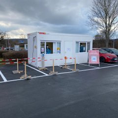 Auf dem Foto sieht man die Teststelle Hornbachparkplatz Lohfelden, weißer Container Absperrungen für Schlangen, im Hinterrund Fahnen.