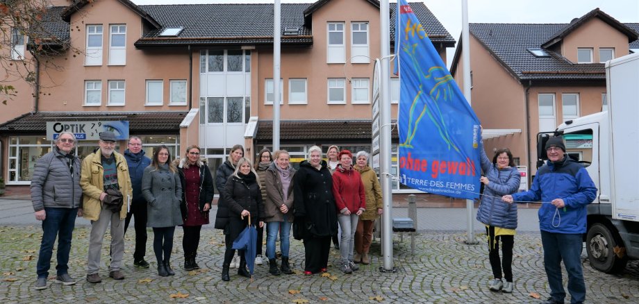 Interne Frauenbeauftragte Sabine Wagner (2.v.r.) und Bürgermeister der Gemeinde Lohfelden, Uwe Jäger (r.), hissten am 25.11. gemeinsam mit anderen Gästen der Veranstaltung die Fahne „Frei leben – ohne Gewalt“ als Zeichen zur Beseitigung von Gewalt gegen Frauen auf dem Dr.-Walter-Lübcke-Platz vor dem Rathaus.
