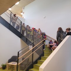 Auf dem Foto sind die Kinder zu sehen, wie sie nach ihrer Ankunft gemeinsam mit ihren Erzieherinnen den hellen, freundlichen Treppenaufgang inspizieren.
