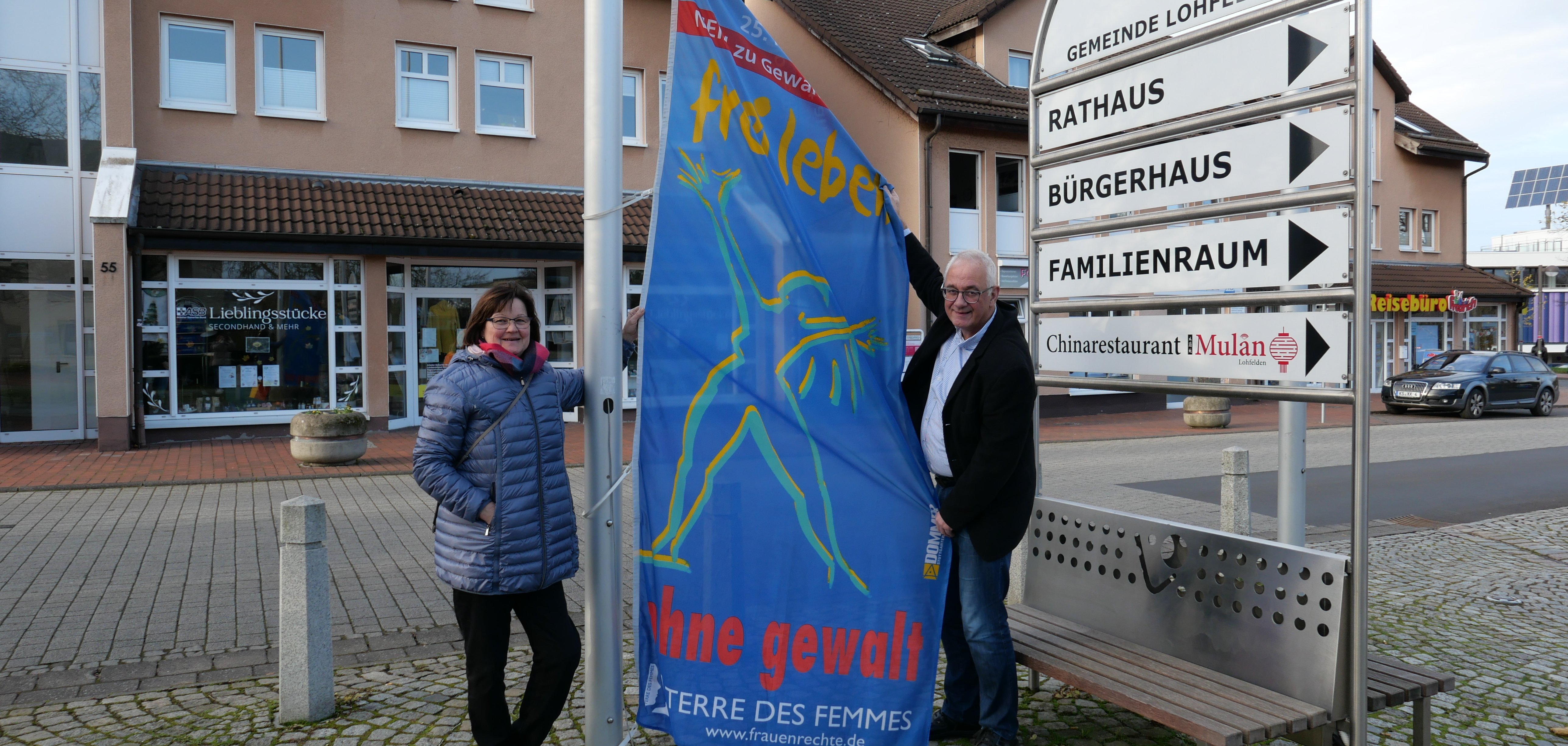 Interne Frauenbeauftragte, Sabine Wagner (l.), und Bürgermeister der Gemeinde Lohfelden, Uwe Jäger, hissten am 25.11. die Fahne „Frei leben – ohne Gewalt“ als Zeichen zur Beseitigung von Gewalt gegen Frauen auf dem Dr.-Walter-Lübcke-Platz vor dem Rathaus.