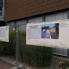 Bauzaun mit Banneren, auf denen Fotos aus 1970 vergrößert angeschaut werden können.