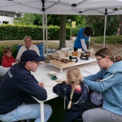 Mit Holz bastelnde Kinder unter einem weißen Pavillon an einem großen.