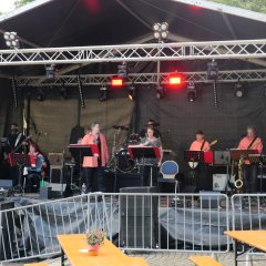 Musikerinnen und Musiker eines Orchesters in roten T-Shirts auf der Bühne.