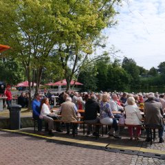 Menschen auf Bierzeltgarnituren am See.