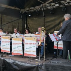 Musikerinnen und Musiker in Rot mit Instrumenten auf der Bühne.