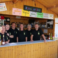 Gruppenbild mit Mitgliedern des Premiereclubs schauen aus der Verkaufshütte aus Holz.