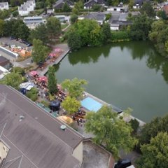 Aufnahme des Festgeländes aus der Luft mit Rathaus, großer bestuhlter Seeterrasse und See mit Insel.