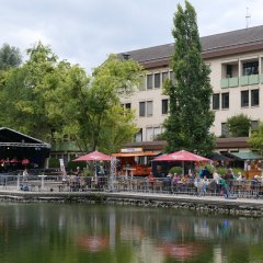 Blick über den See auf bestuhlte Seeterrasse mit Rathaus im Hintergrund.