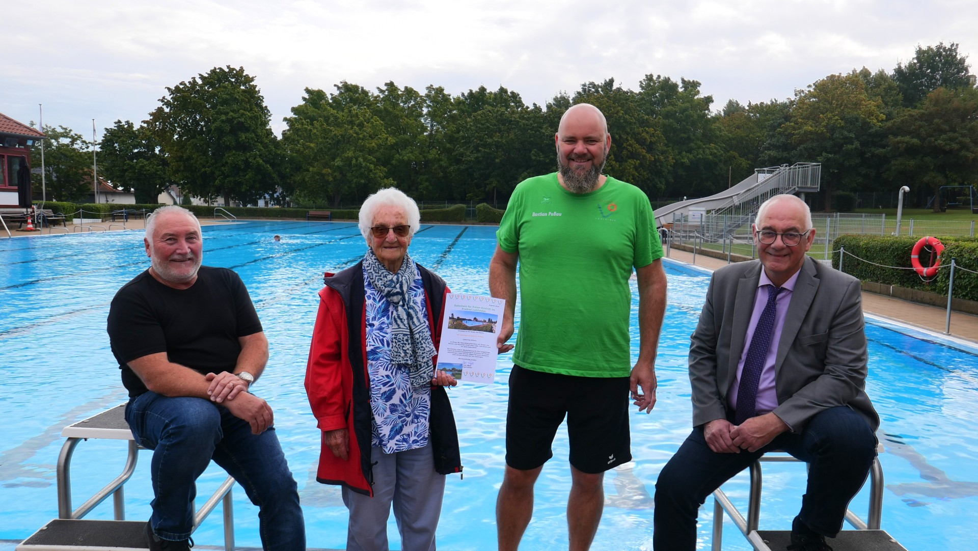 Bürgermeister Uwe Jäger steht gemeinsam mit der Jubilarin und den beiden Schwimmmeistern vor dem Schwimmbecken im Freibad Lohfelden.