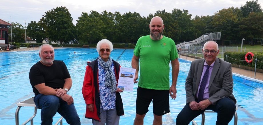 Bürgermeister Uwe Jäger steht gemeinsam mit der Jubilarin und den beiden Schwimmmeistern vor dem Schwimmbecken im Freibad Lohfelden.