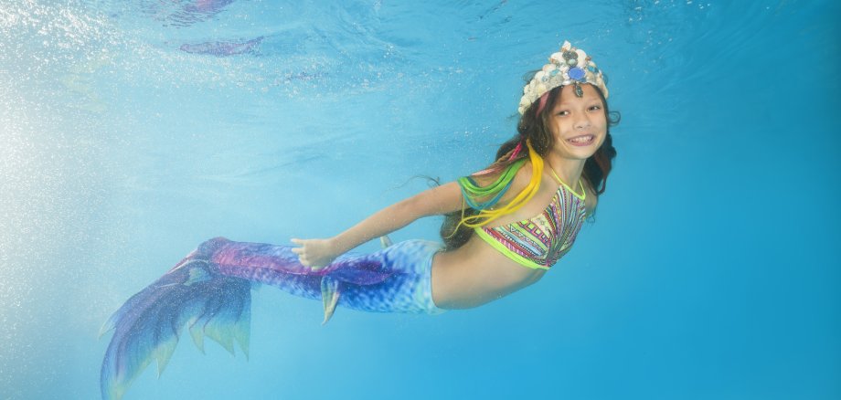 A girl in a mermaid costume poses underwater in a pool. Young beautiful girl poses underwater in the pool.
