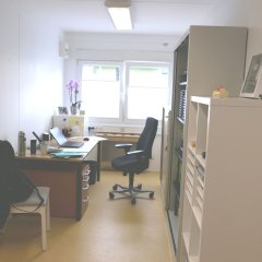 Container-Anlage - Blick in ein Büro mit Schreibtisch, Stuhl, Regal und 2 Fenstern