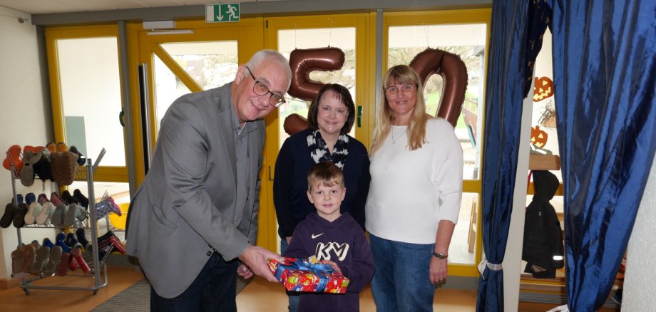 Bürgermeister Uwe Jäger übergibt gemeinsam mit Tanja Hammer, Leiterin des Sachgebiets Kindertagesstätten (M.), und komm. Leiterin der KiTa Ochshausen, Sandra Schiffmann, eines der Geschenke stellvertretend für alle Kinder der KiTa Ochshausen an Vorschulkind Lukas