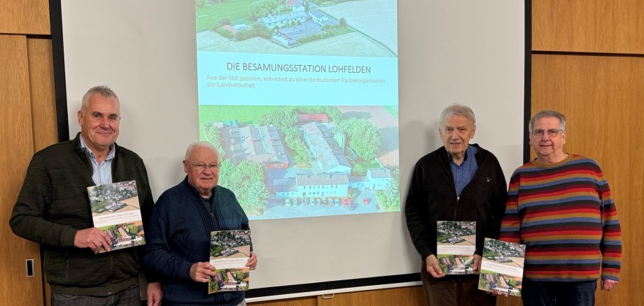 Freuten sich am 19.11. die neue Publikation „Die Besamungsstation Lohfelden“ vorstellen zu dürfen (v.l.n.r.): Herbert Brethauer, Sprecher der Geschichtswerkstatt, gemeinsam mit den Mitgliedern der Geschichtswerkstatt Walter Pfaffe, Dr. Hans-Josef Müther, Tierarzt der Besamungsstation Lohfelden, und Eberhard Ullrich. Vier Männer höheren Alters in Freizeitkleidung stehen vor einer Beamer-Leinwand auf der das Foto der Besamungsstation Lohfelden projiziert ist; jeder der vier Herren hält ein Buch über die Besamungsstation Lohfelden in der Hand.