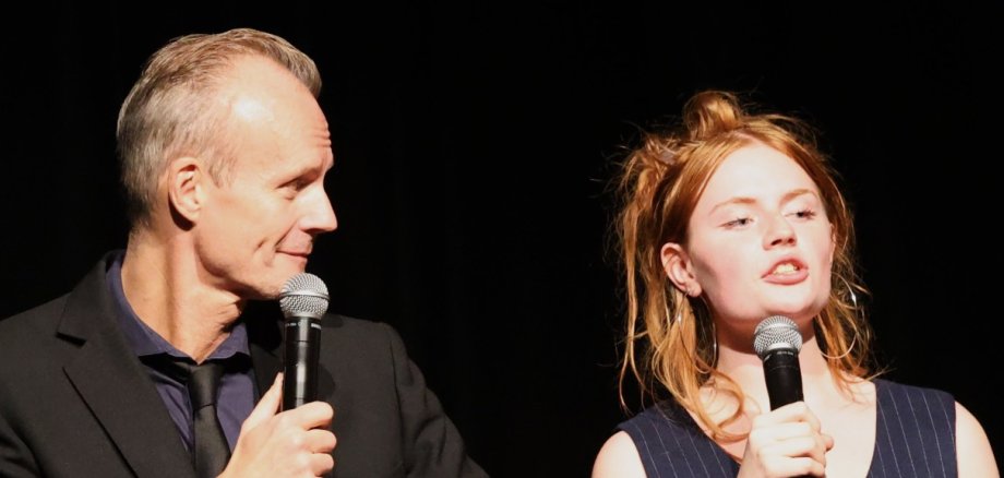 Kabarett in Lohfelden Max Uthoff - mit Mikrophon in der Hand - lächselt seiner Tochter Toni, ebenfalls mit Mikrophon zu, während sie redet.