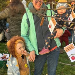 Die Eltern befestigen die Namenskärtchen ihrer Kinder im Apfelbaum. Sophie Neugebauer freut sich über den Apfelbaum  und das Kärtchen für ihre kleine Tocher Emmi, daneben ihr Sohn Hannes.