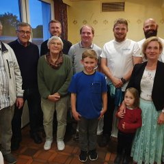 Eine Gruppe bestehend aus elf Frauen und Männern verschiedenen Alters sowie zwei Kindern steht nebeneinander im Gastraum eines Restaurants. 