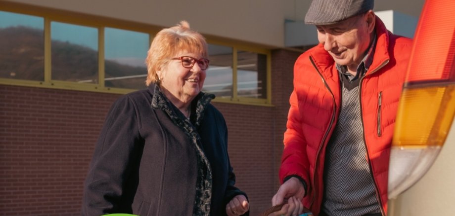 Mann hilft älterer Dame den Einkauf in das Auto zu stellen