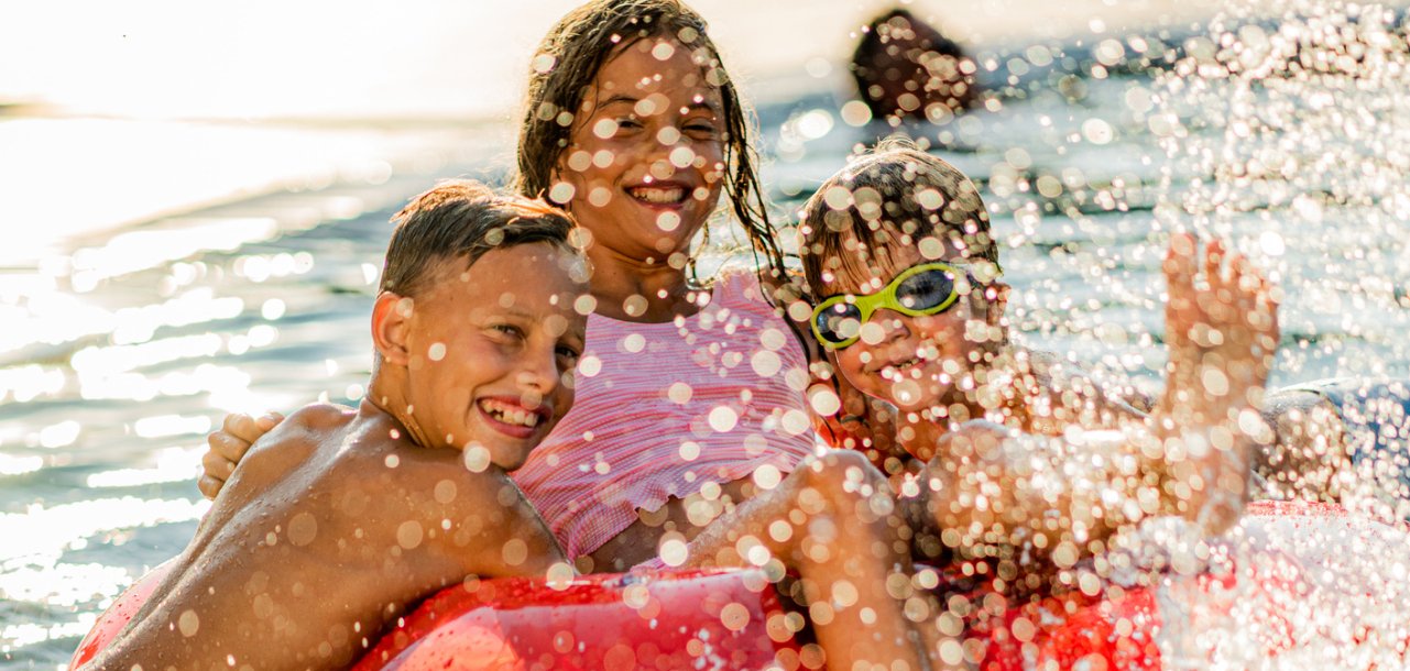 Kinder planschen im Wasserbecken mit Luftmatratze und lachen fröhlich