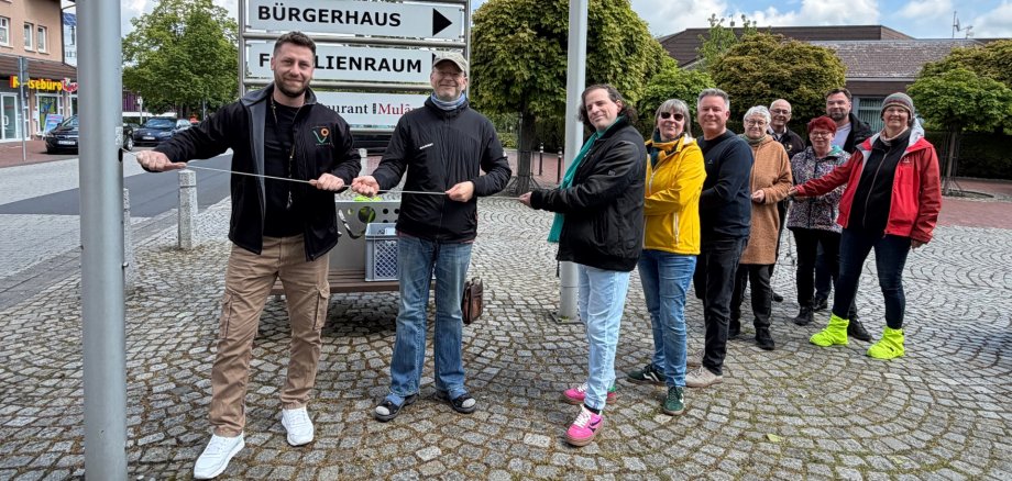 Hissen der Regenbogenfahne. Mehrere Personen ziehen am Seil, das die Regenbogenfahne am Fahnenmast nach oben bringt.