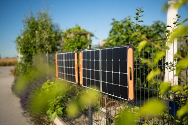 Tragbare Solarmodule, die an einem sonnigen Tag mit blauem Himmel an einem privaten Gartenzaun hängen, um nachhaltige grüne Energie zu erzeugen