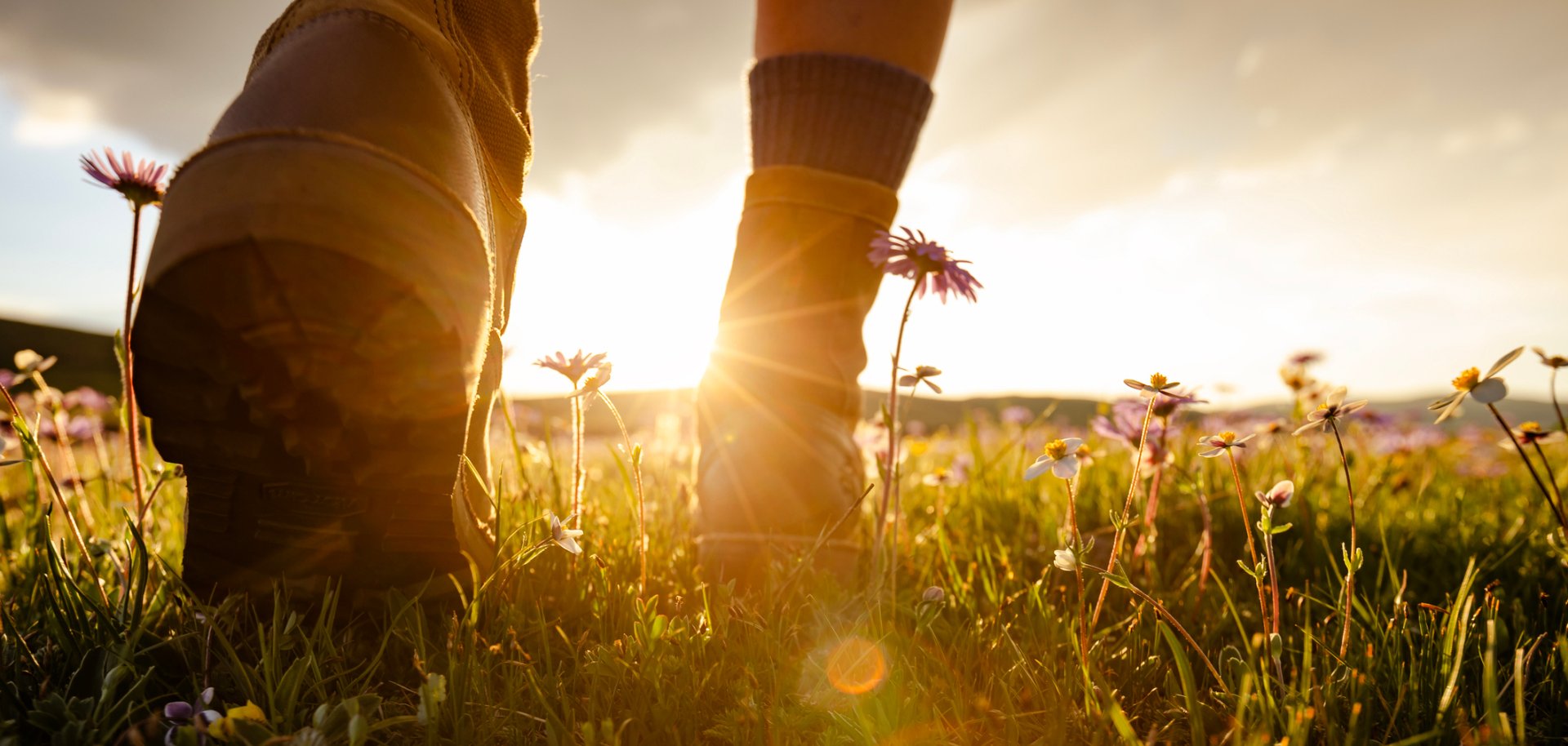 Detailperspektive von Wanderschuhen einer Wanderin, die in den Sonnenuntergang läuft.