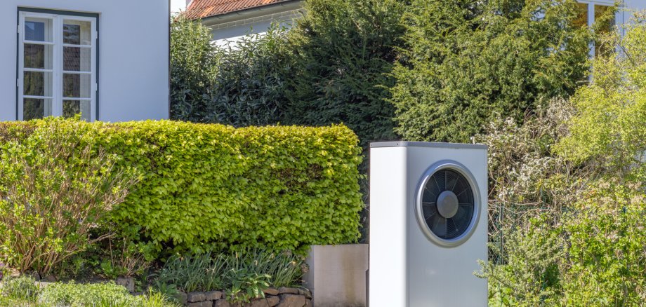 Ansicht einer Wärmepumpe im Garten vor einem Einfamilienhaus Ansicht einer Wärmepumpe im Garten vor einem Einfamilienhaus