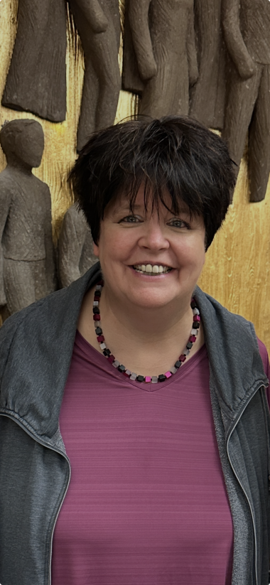 Ingrid Kühne mit schwarzen Haaren vor der Bürgerinnen- und Bürger-Skulptur vor goldenem Hintergrund im Foyer des Lohfeldener Bürgerhauses.
