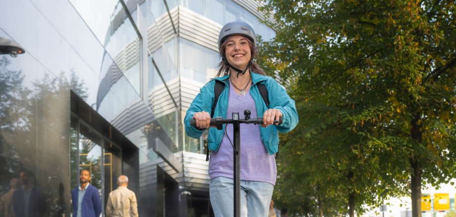 Junge Frau mit Helm fährt mit einem E-Scooter durch die Stadt