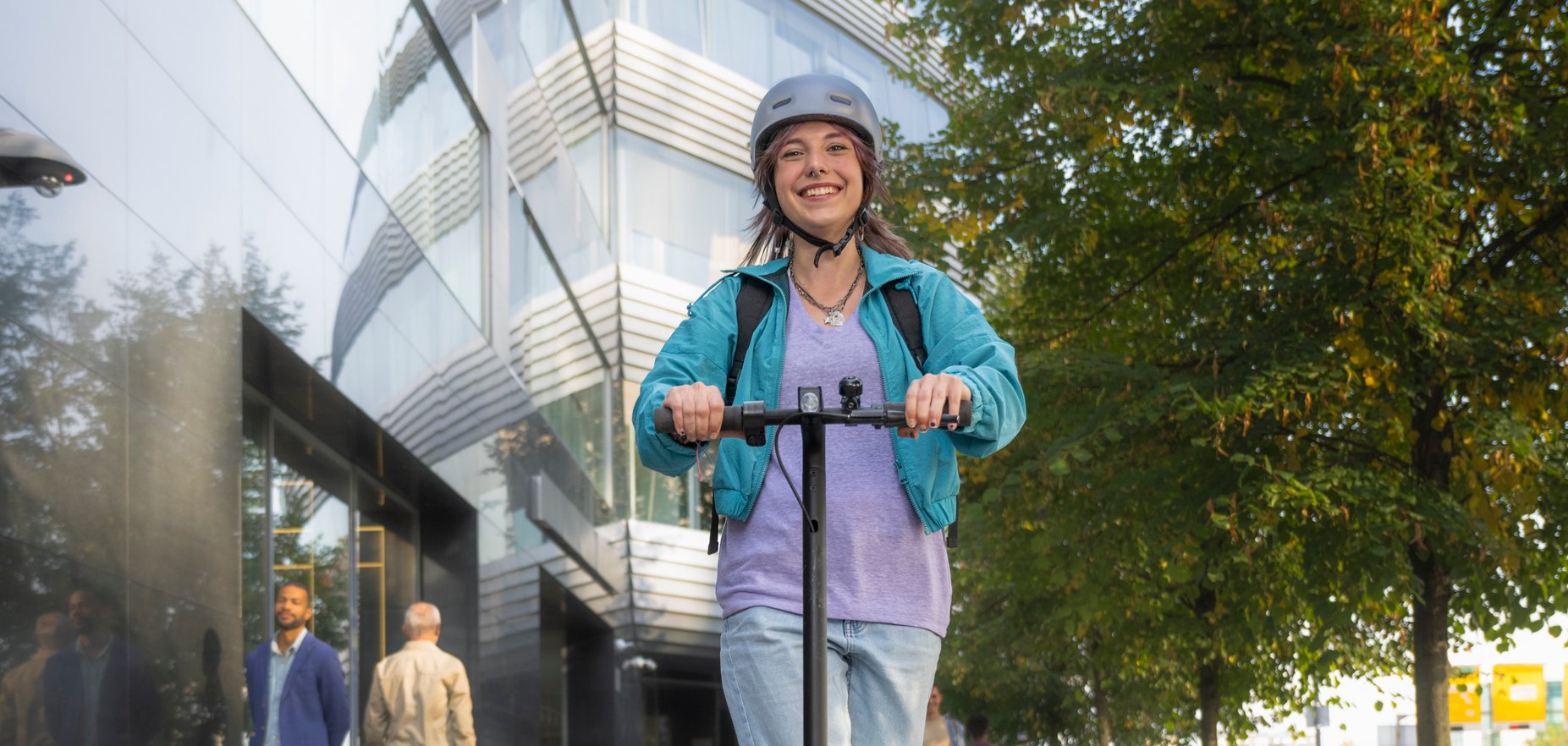 Junge Frau mit Helm fährt mit einem E-Scooter durch die Stadt