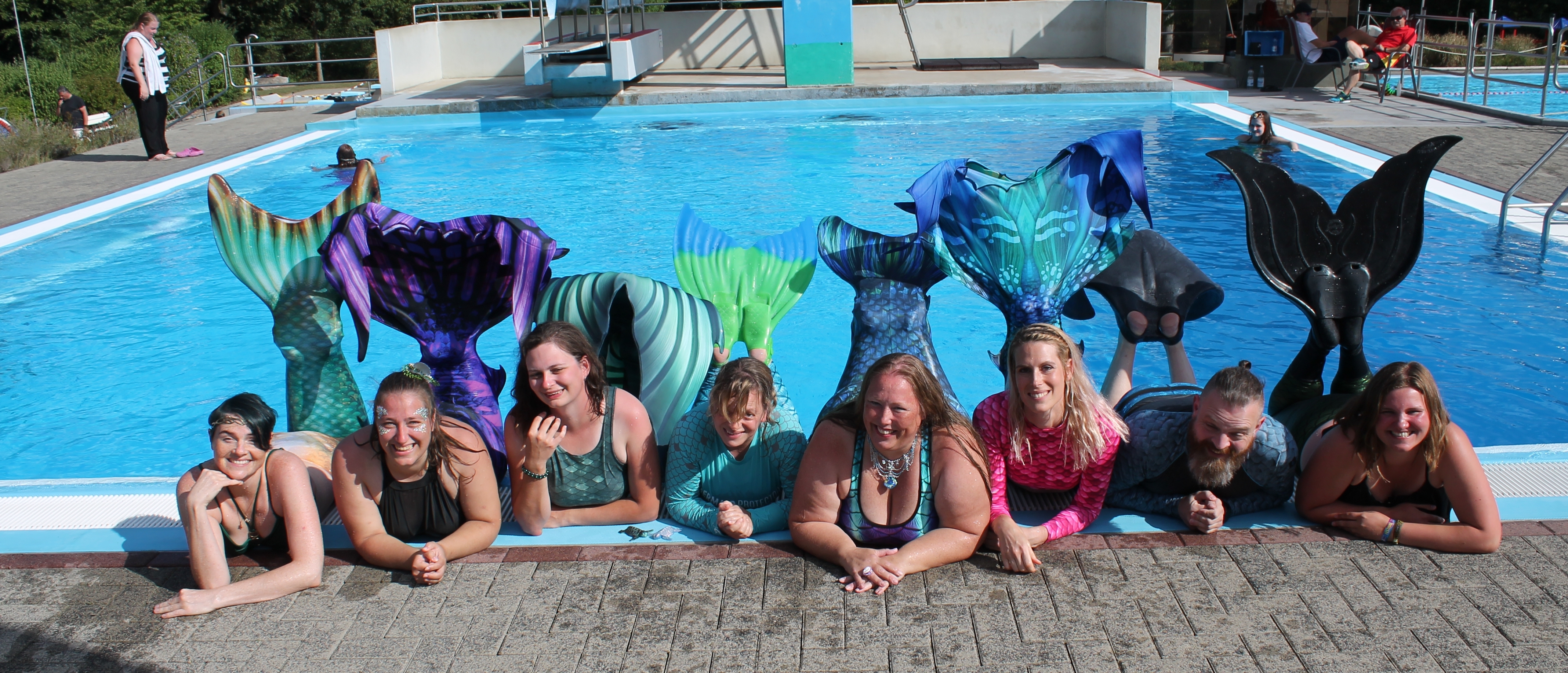 Merfolk - Mehrjungfrauen Mehrjungfragen vor einem Schwimmbecken.