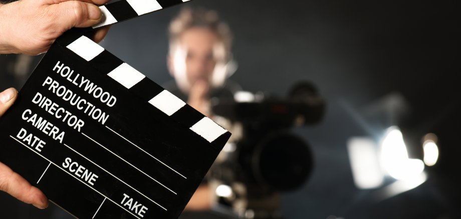Auf dem Foto sieht man im Vordergrund eine schwarz-weiße Filmklappe. Im unscharfen Hintergrund ist ein Junge zu erkennen.