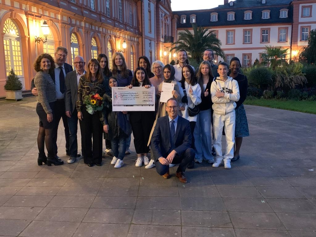 Teslihan Ayalp, Integrationsbeauftrage der Stadt Kassel (l.), Thomas Ackermann, hauptamtlicher Kreisbeigeordneter (2.v.l.) und Minister Kai Klose (vorn kniend) freuen sich mit der Gruppe nach der Preisverleihung im Schloss Biebrich.   