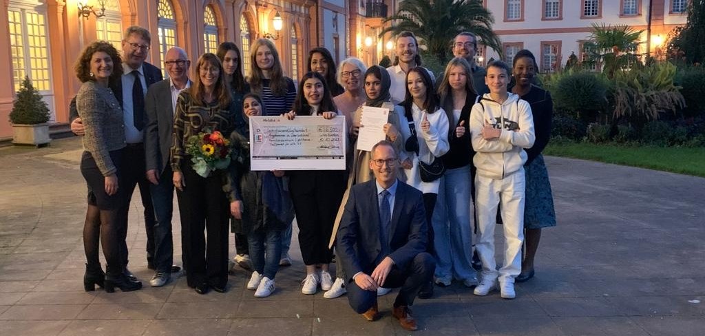 Teslihan Ayalp, Integrationsbeauftrage der Stadt Kassel (l.), Thomas Ackermann, hauptamtlicher Kreisbeigeordneter (2.v.l.) und Minister Kai Klose (vorn kniend) freuen sich mit der Gruppe nach der Preisverleihung im Schloss Biebrich.   