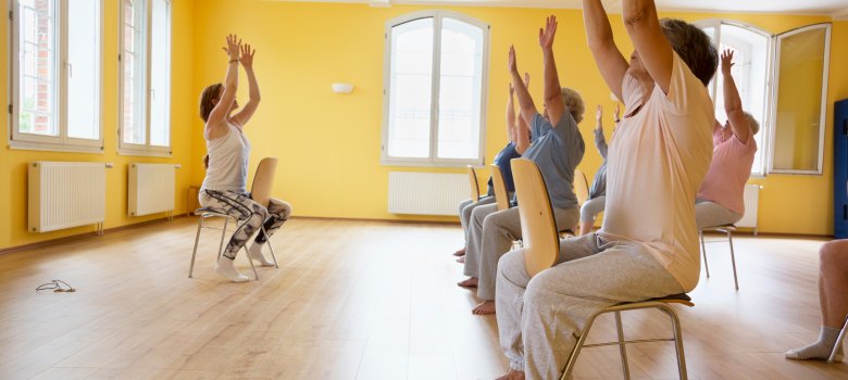 Teacher and active senior women yoga class on chairs